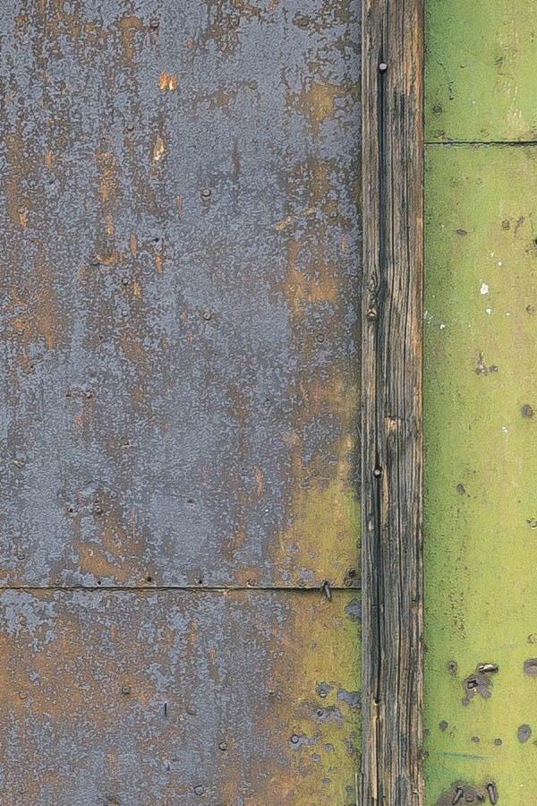 Photo 25763: Decayed gate of unpainted boards covered by yellow, light green, orange, brown and black metal plate