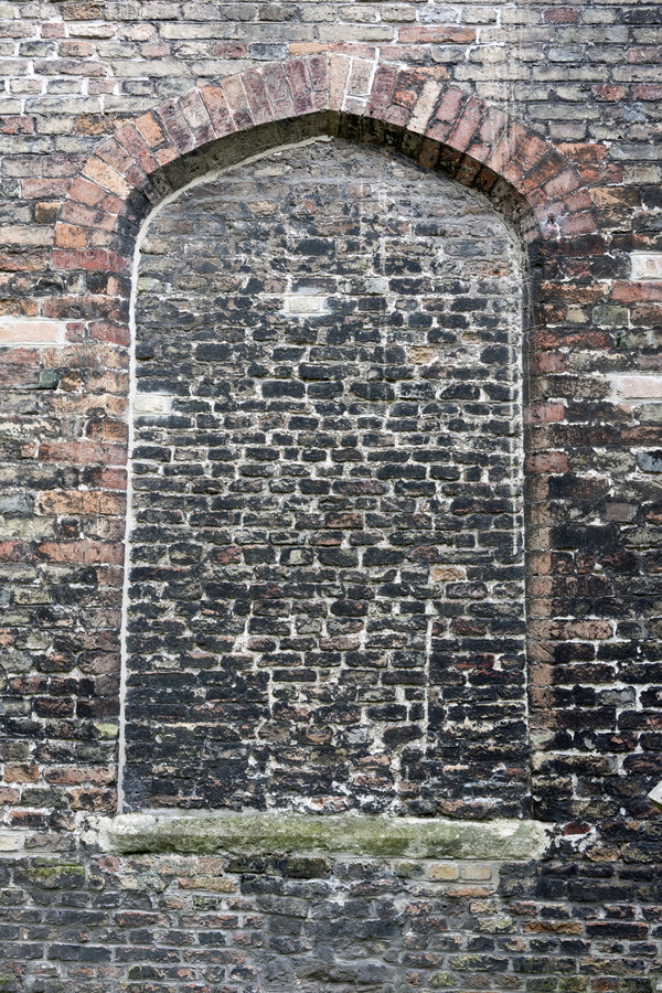 Photo 15908: Worn wall of black, yellow and red bricks with indentation