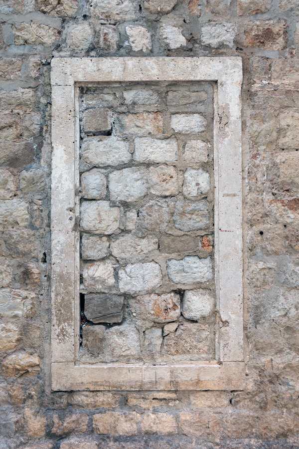 Photo 26268: Worn, grey stone wall with a window frame blocked by more stones