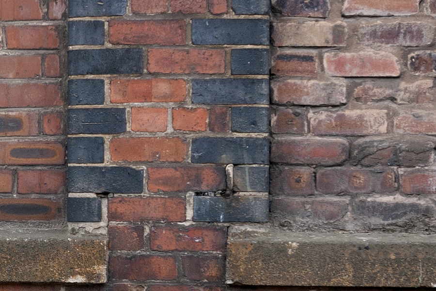 Photo 11614: Worn, red and black brick wall with three indentations